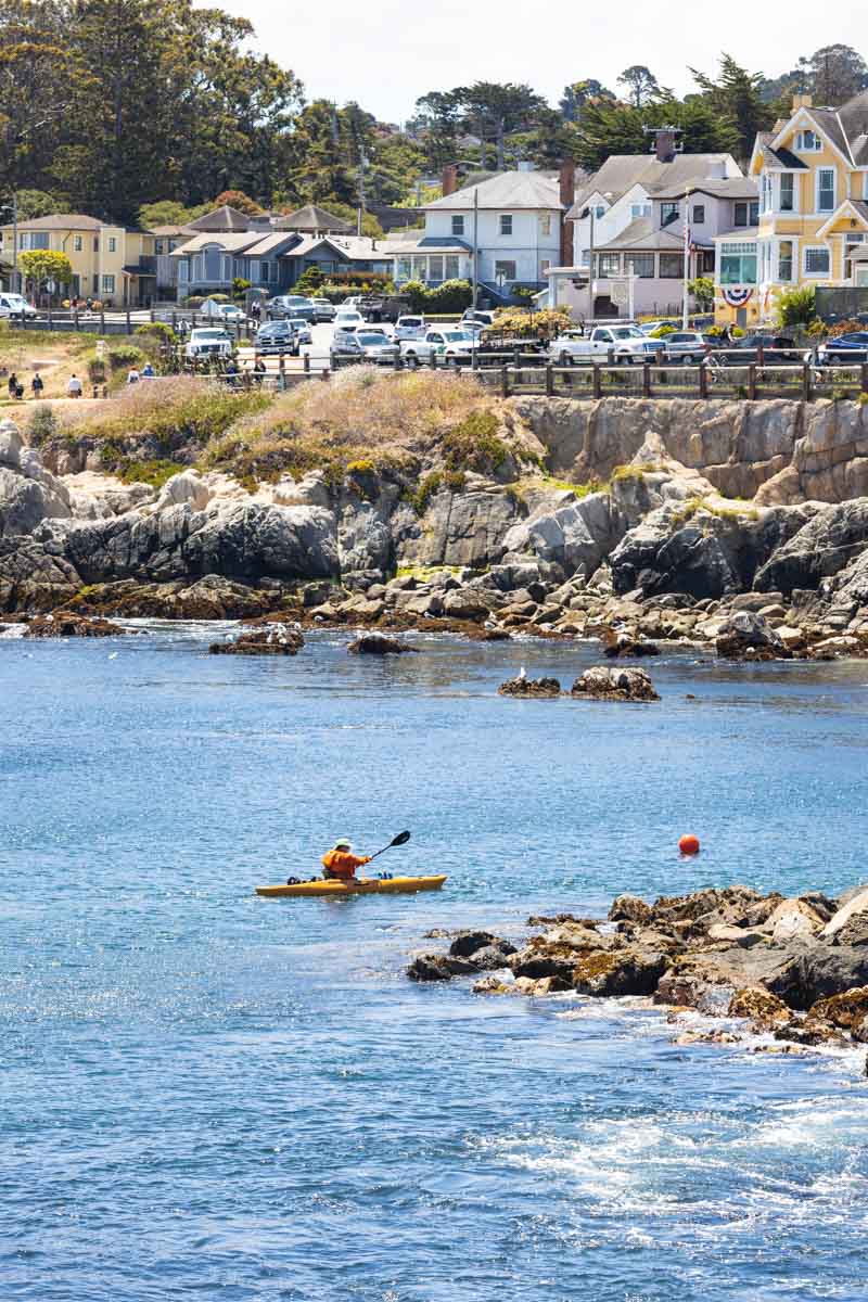A man on a yellow kayak navigating the coastline around Lovers Point Park.