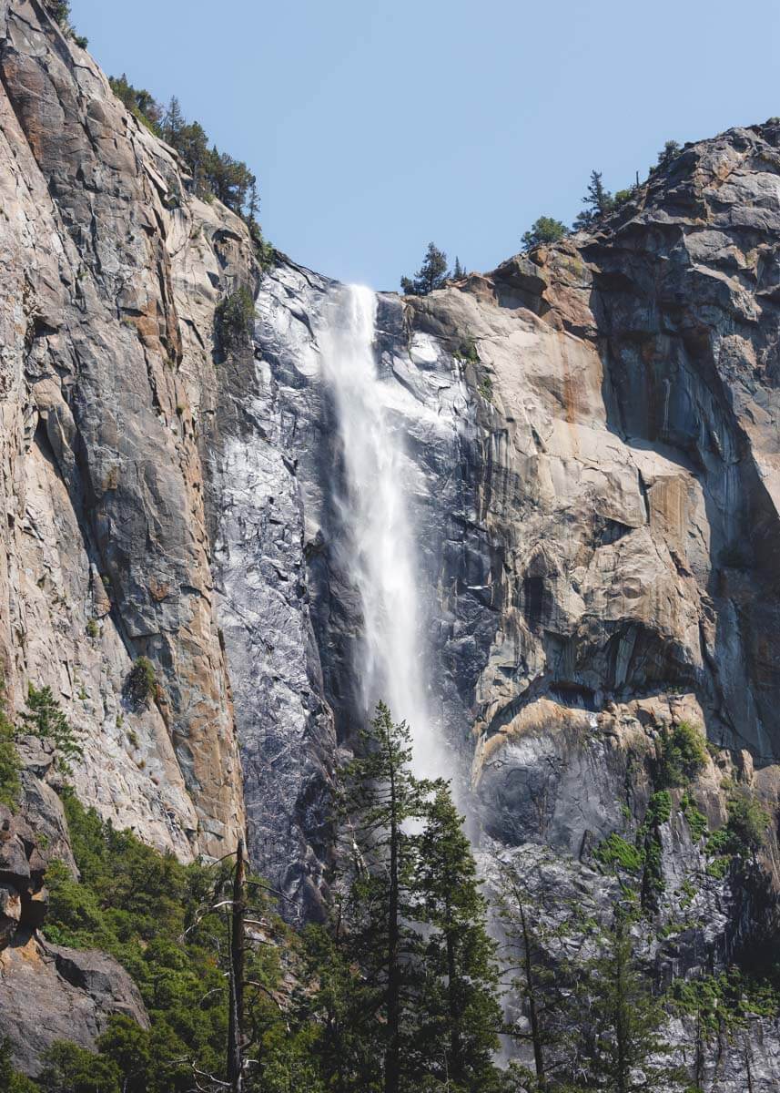 The huge cascade of Bridalveil Falls appearing from the top of a cliff and falling to the trees below.