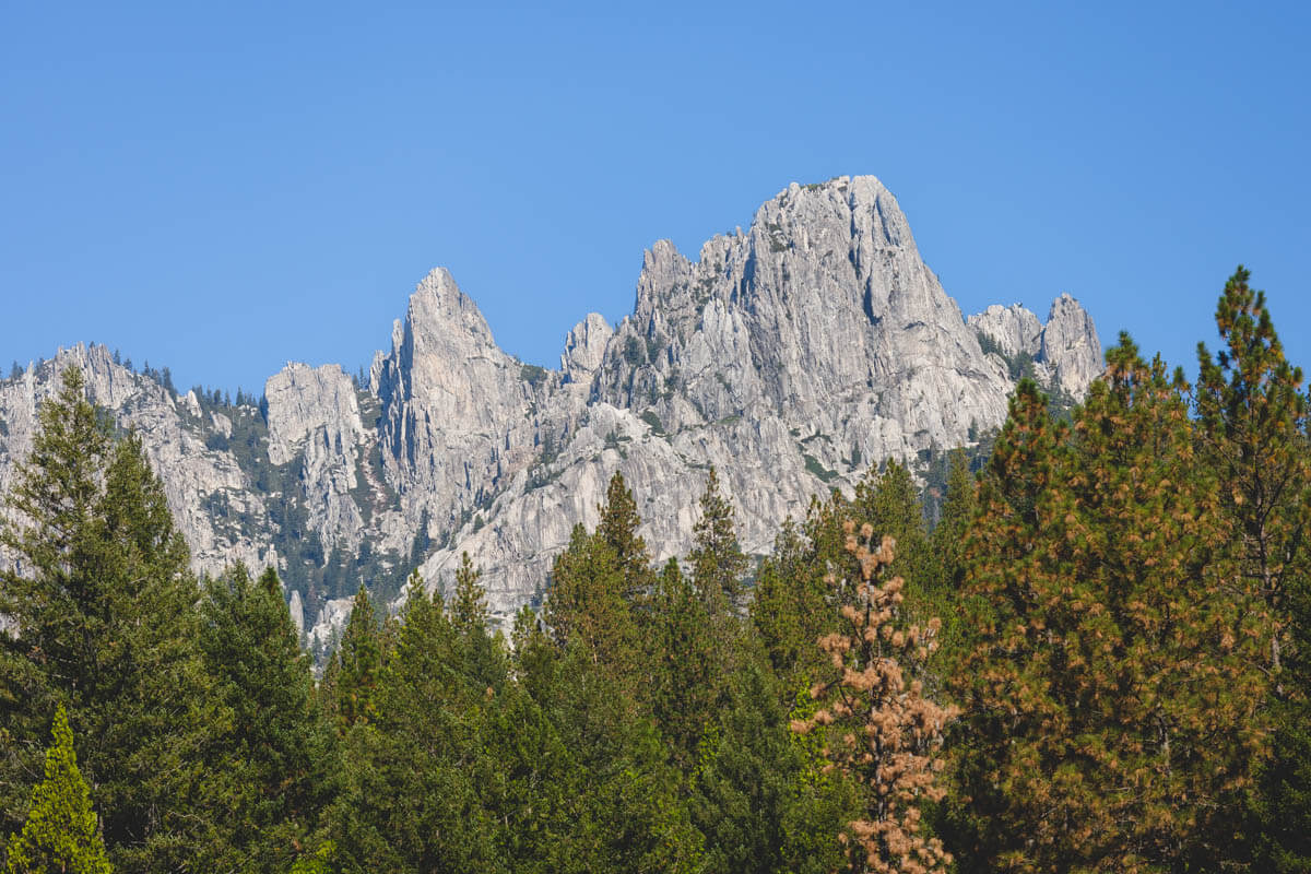 The Castle Crags rock formations see over the trees from a distance on a sunny day.