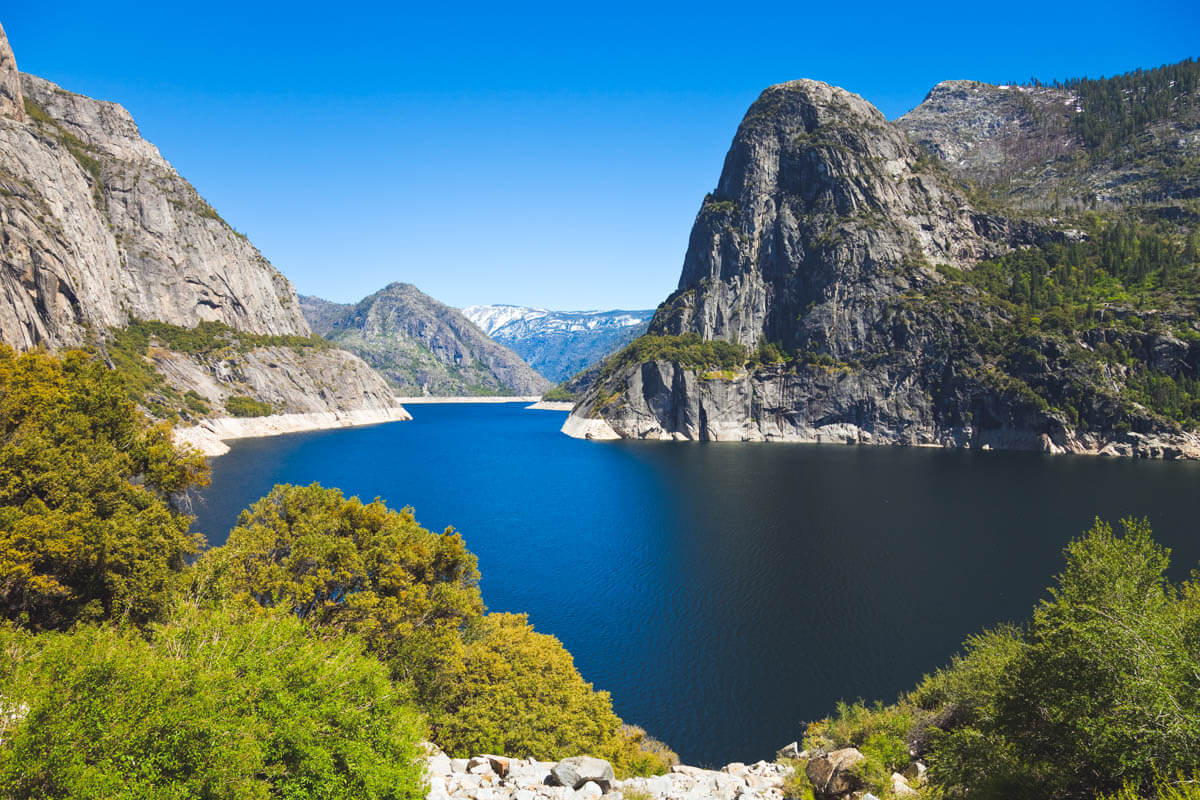 The huge lake of Hetch Hetchy reservoir surrounded by mountains on a sunny day.