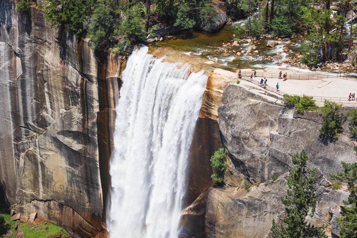 Tourists standing on a clifftop viewing platform over the huge cascade of Vernal Falls in Yosemite.
