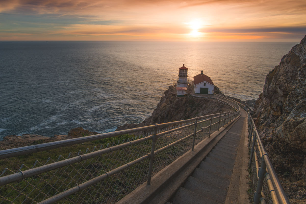 A staircase leading down to Point Reyes Lighthouse with a bright red sunset behind.