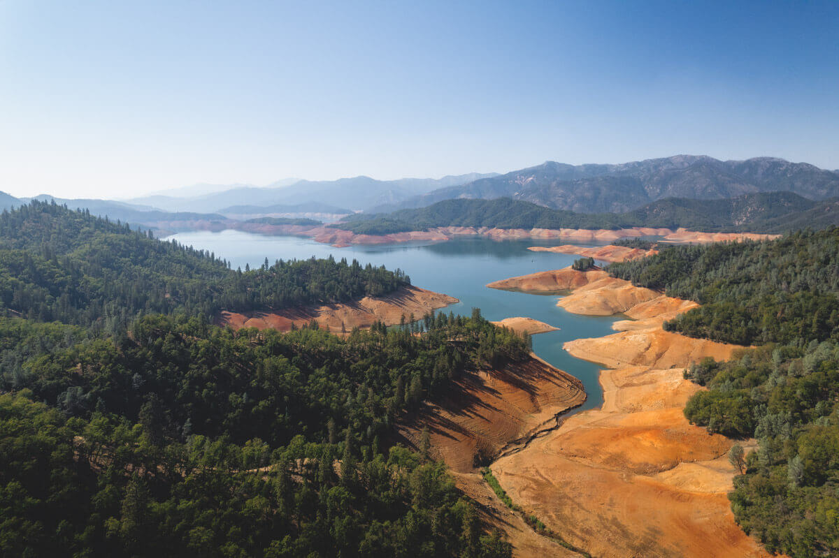 Aerial view of Shasta Lake nestled in between forests and orange cliffs. 