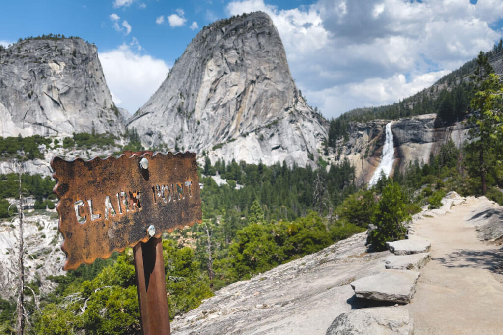 Clark Point trailhead sign with a view of Nevada Falls in the distance.