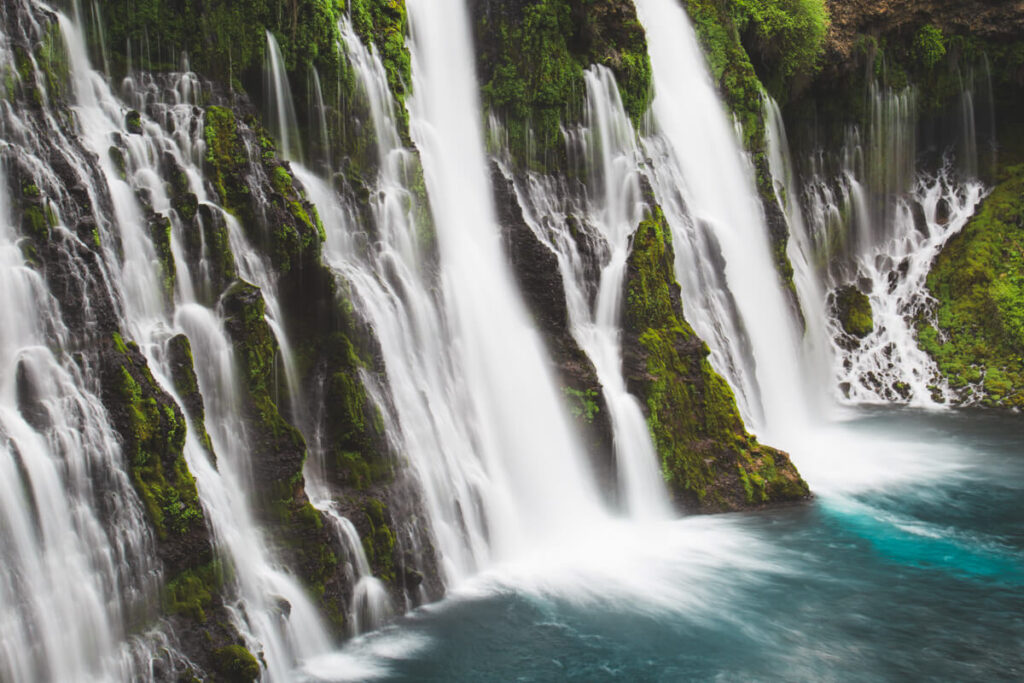 Silky cascades of Burney Falls surrounded by bright green moss and a deep blue plunge pool.