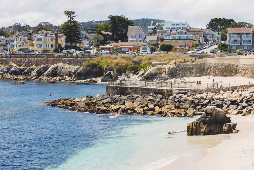 Tourists walking along a beach with Monterey local houses in the background.