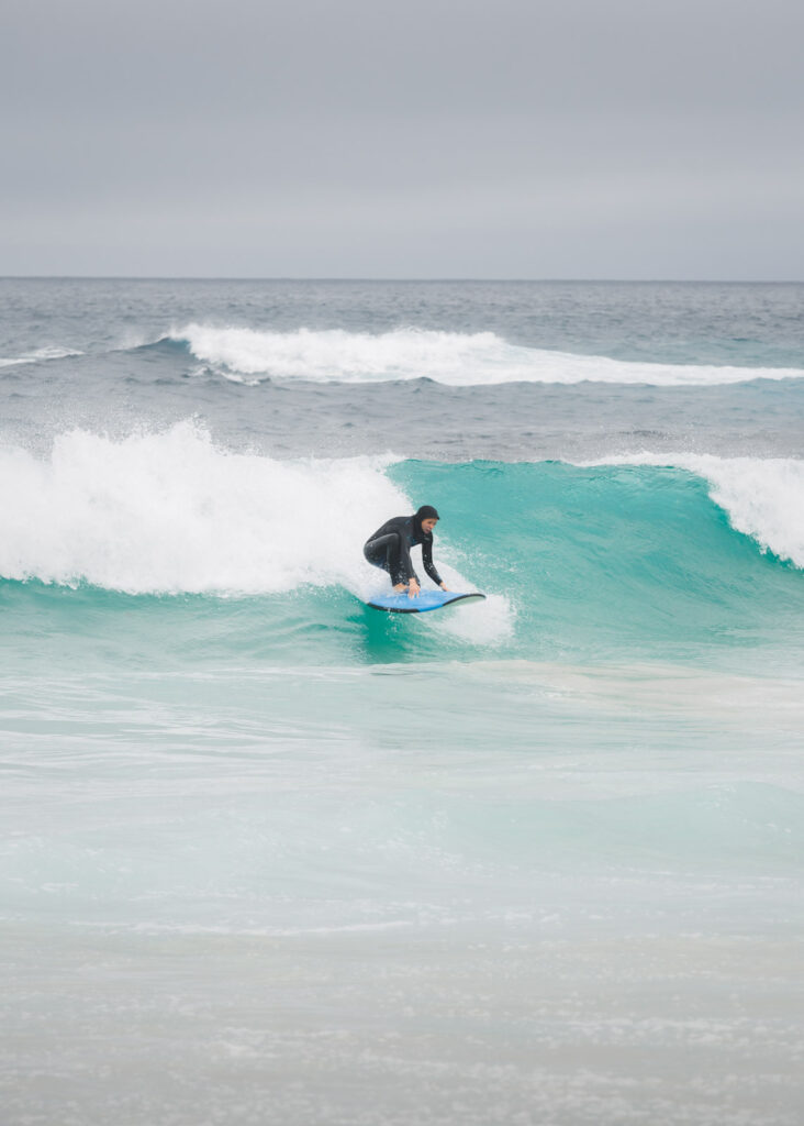A surfer attempting to stand while surfing on the baby blue waters of Asilomar Beach.