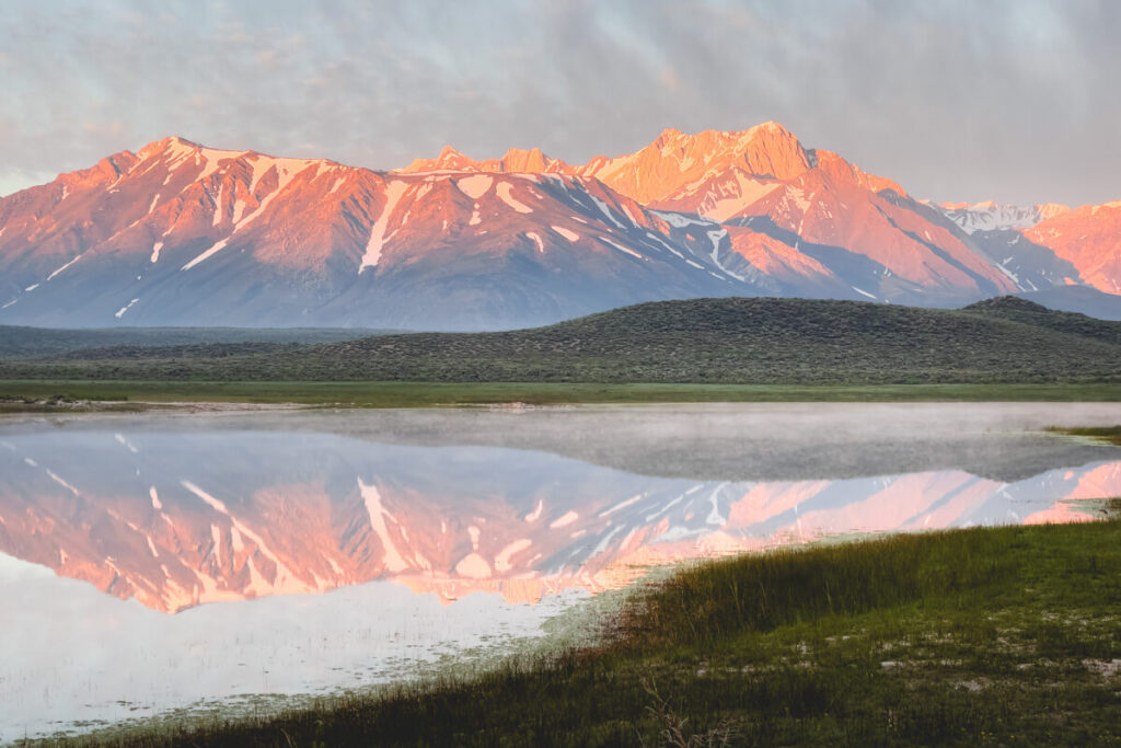 The Eastern Sierra Nevada mountains being reflected on a still lake at sunrise.