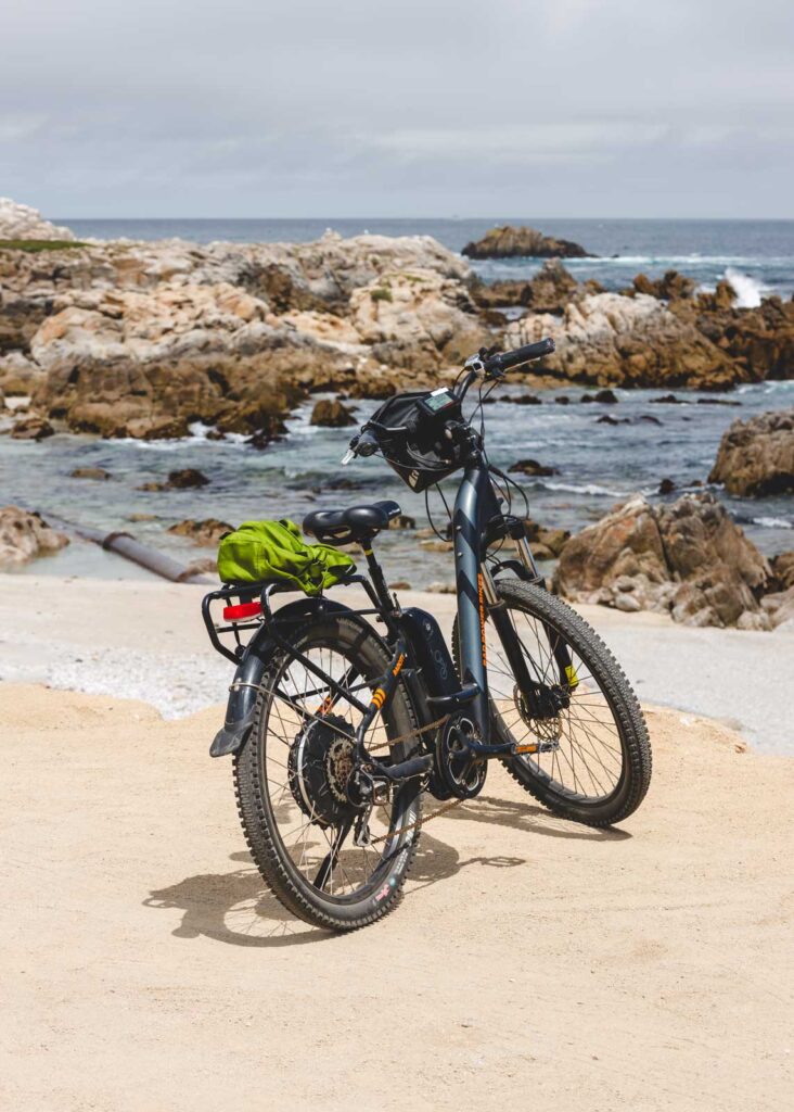 An e-bike on a stand besides an ocean full of rocks on an overcast day.