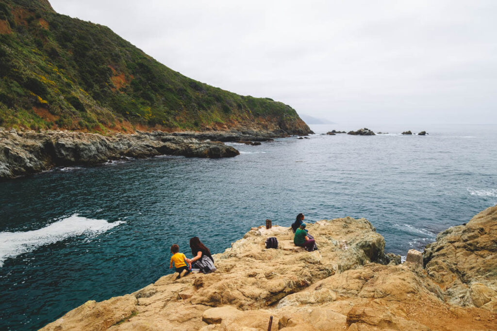 Families resting on the rocks besides the ocean next to Partington Cove.