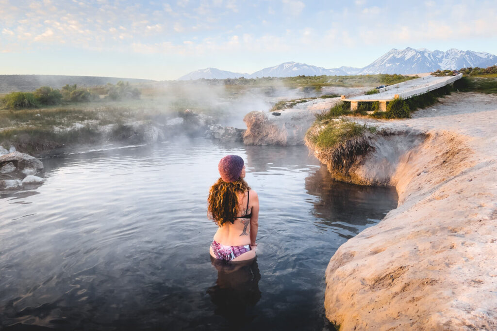 A female tourists bathing in Wild Willy's Hot Springs with a mountain view in the distance.