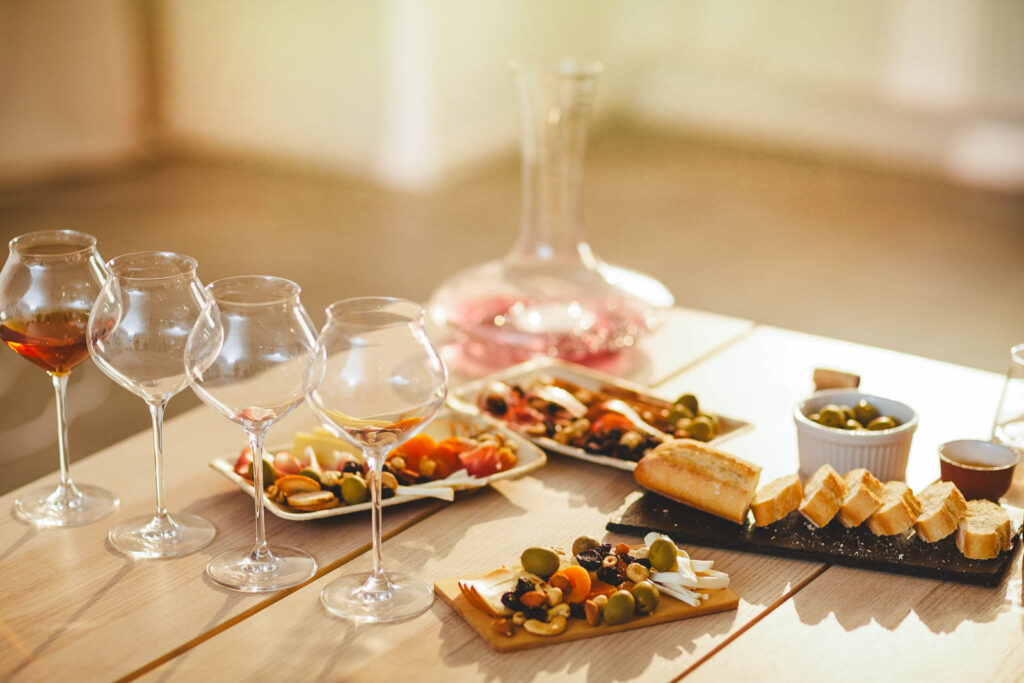 Glasses of wine along with cheese, olive and nuts plates on a wooden table.