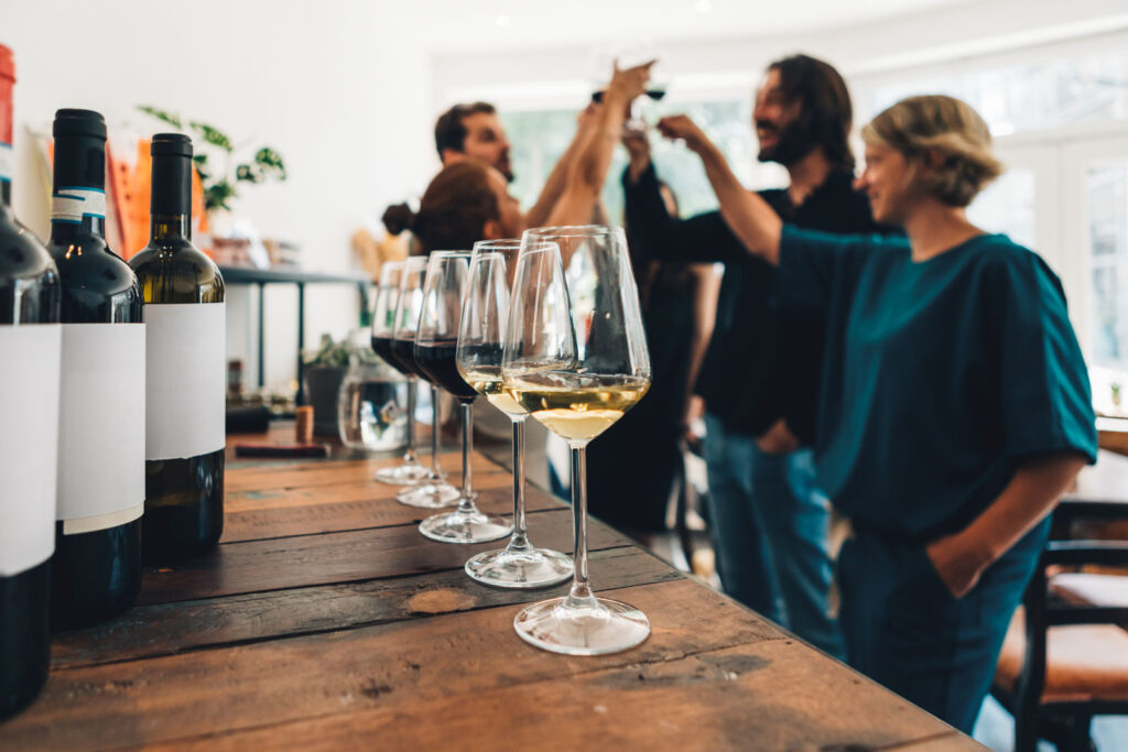 A group cheering glasses in the background with unbranded wines in the foreground.