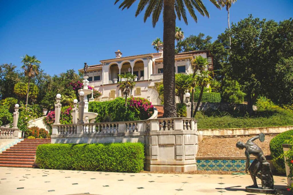 The tropical looking Hearst Castle surrounded by palm trees, bushes and statues.