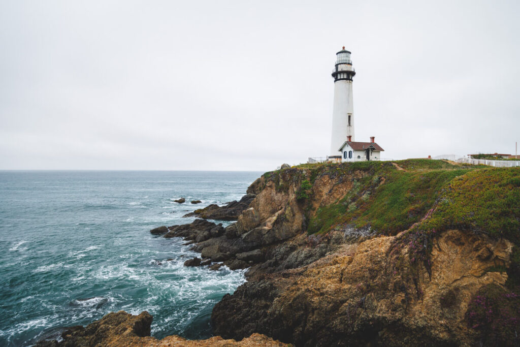 White lighthouse on a headland in Pigeon Point Light Station State Historic Park on an overcast day.