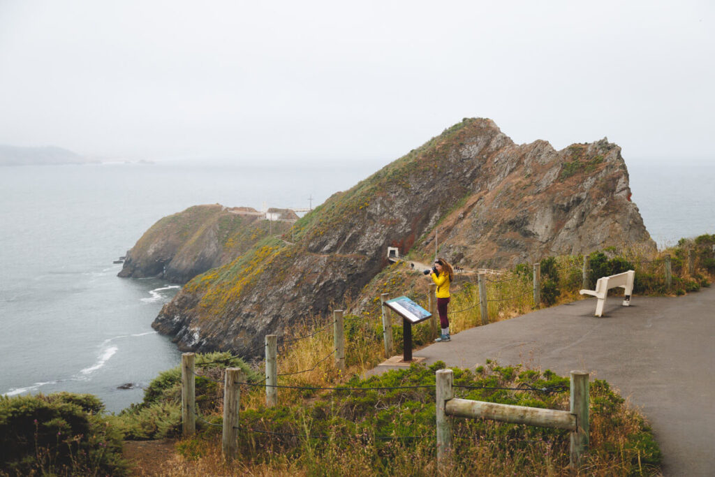 A female photographer taking photos of San Francisco Bay from Point Bonita Lighthouse trail.