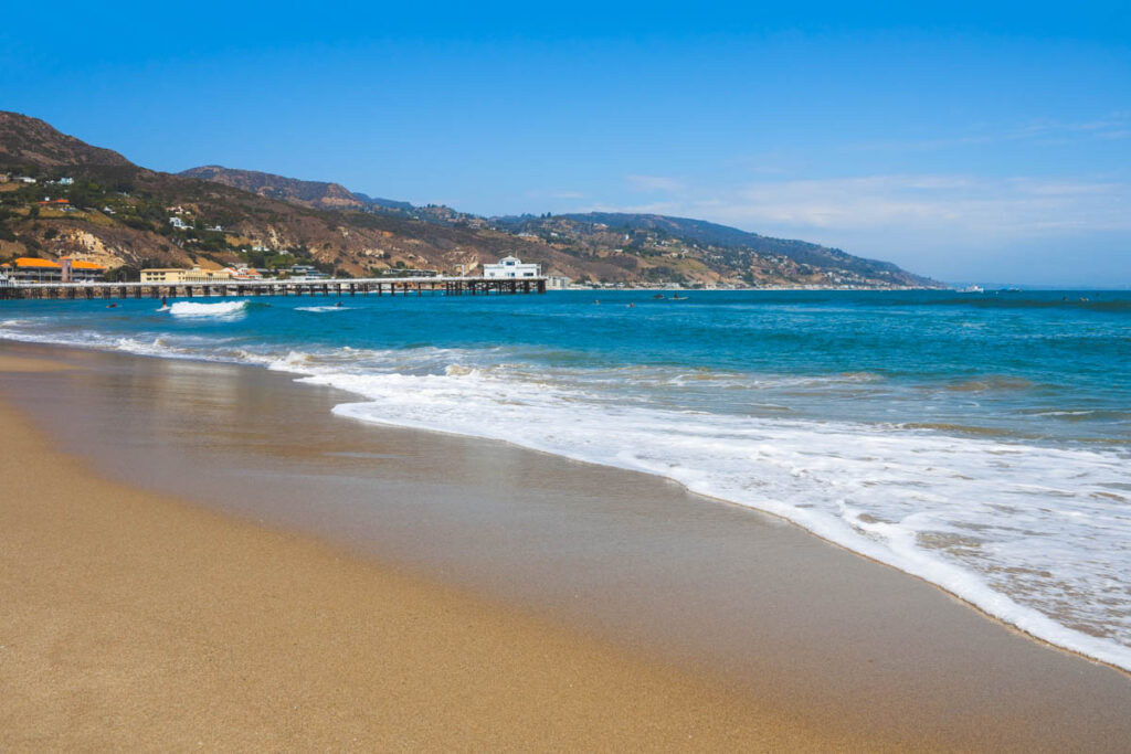 Few tourists out surfing in the water at Malibu Lagoon State Beach on a clear day.