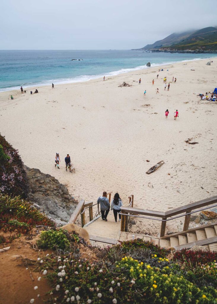 Two people walking down a wooden staircase to reach Garrapata State Beach.