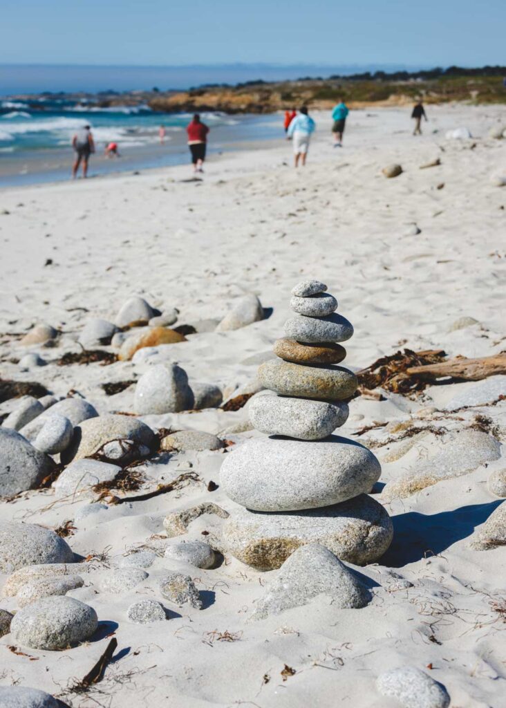 A neat pile of stones on a beach while tourists enjoy their day in the background.