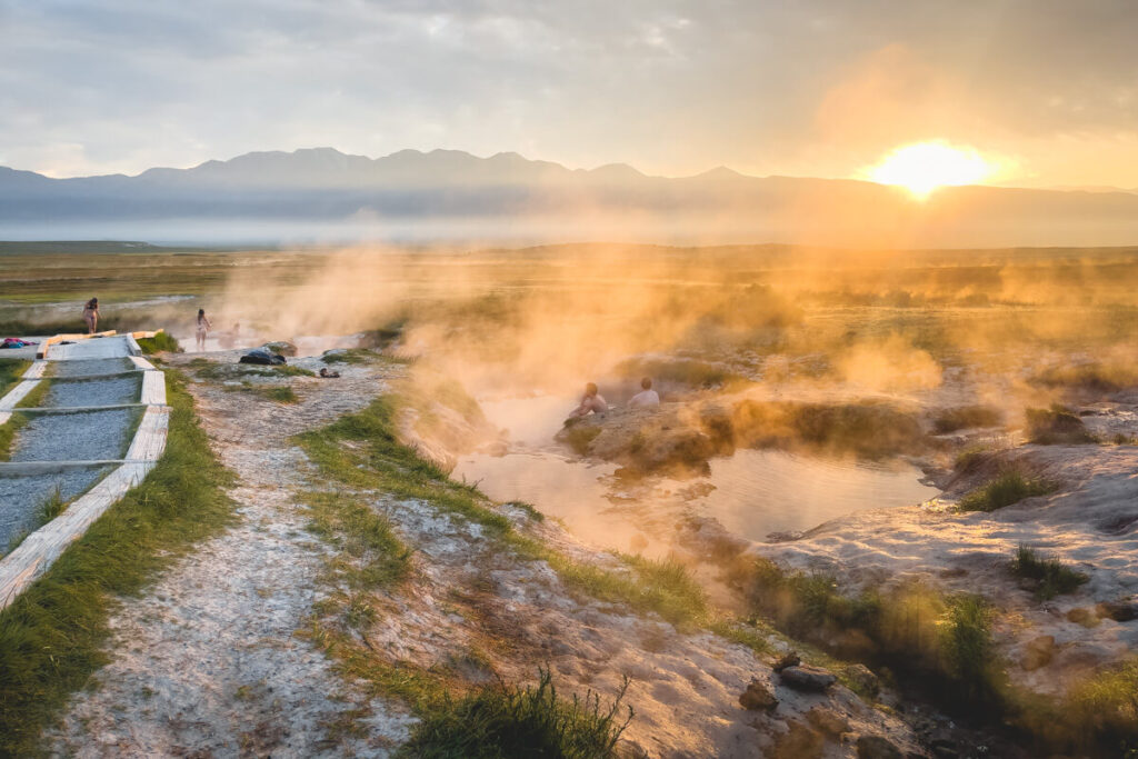 Sunrise over the steaming Wild Willy's Hot Springs while tourists sit in the pools.