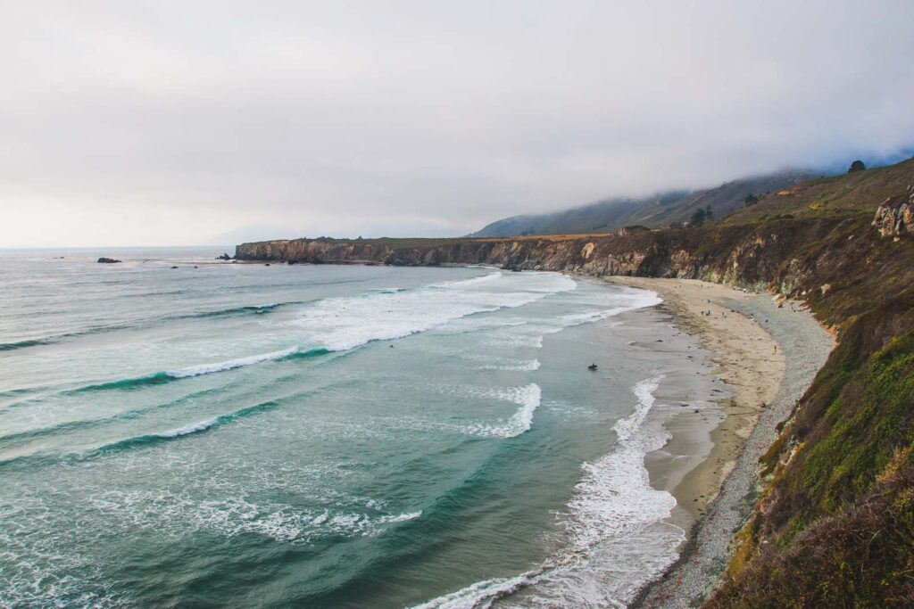 A surfer walking out into the ocean with his surf board in Sand Dollar beach in Big Sur.