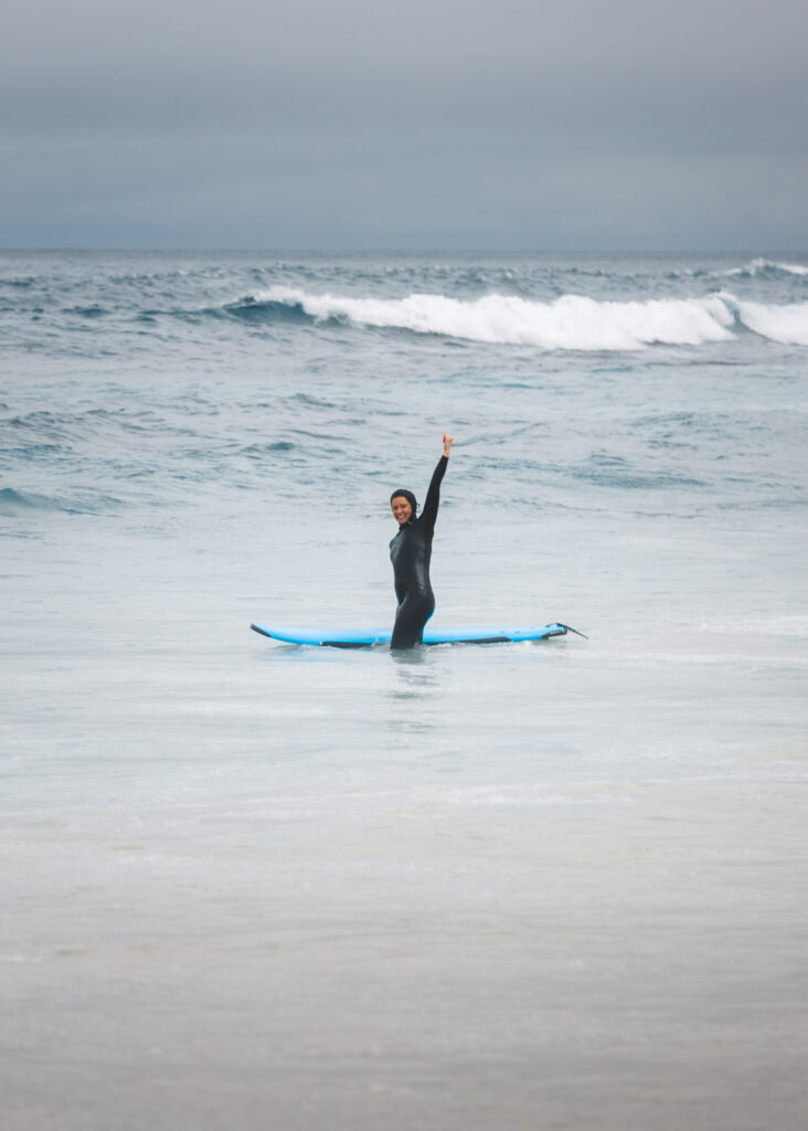 A happy surfer in a wetsuit waving to the camera from the ocean at Asilomar Beach.