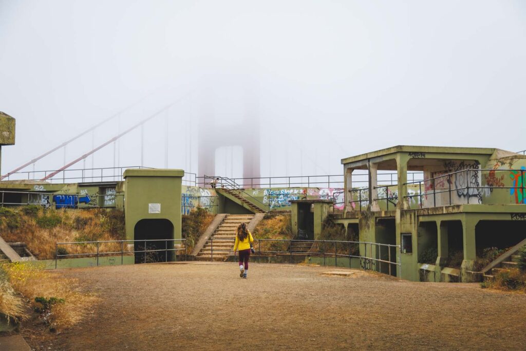 Nina exploring the abandoned looking Battery Spencer with the Golden Gate Bridge in the background.