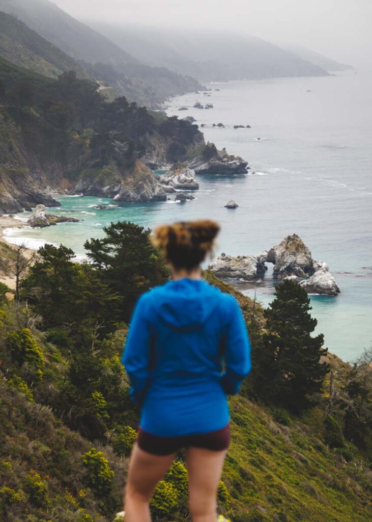 A female hiker looking out over a view of Julia Pfeiffer Burns State Park on an overcast day.