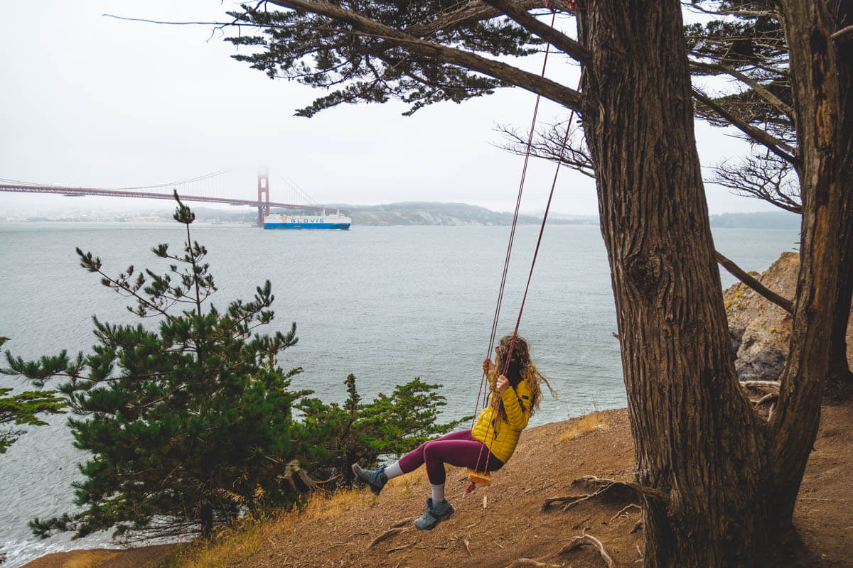 A woman on a tree-swing looking out over San Francisco Bay and the Golden Gate bridge.