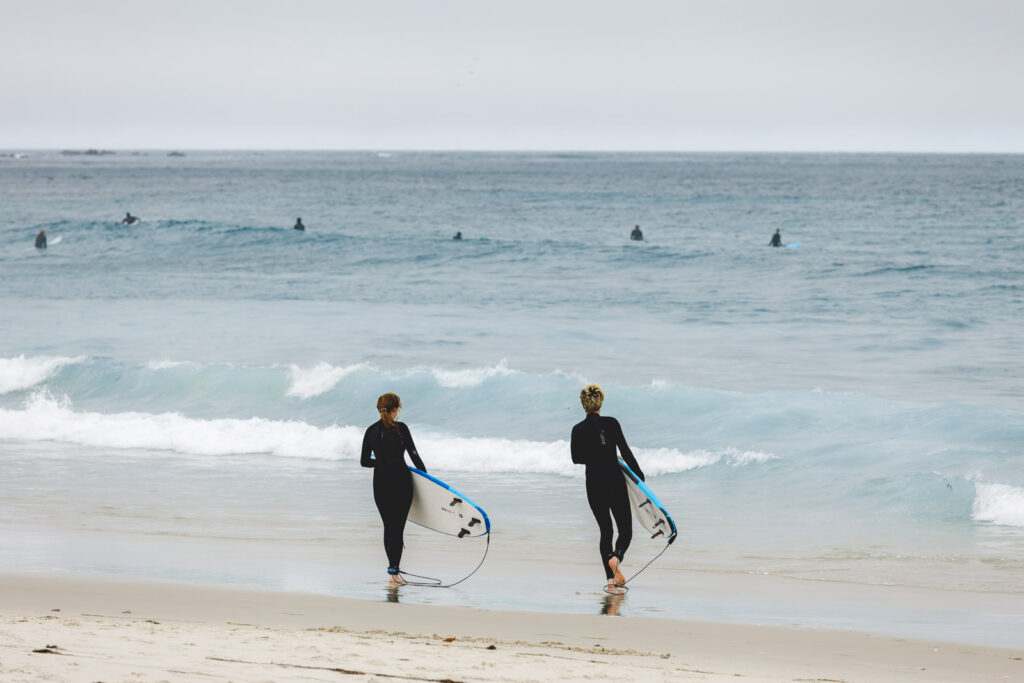 Two surfers in black wetsuits holding surfboards walking towards the ocean at Asilomar Beach.
