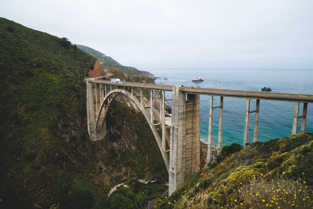 A car towing a caravan over the arched Bixby Bridge along the Big Sur drive.