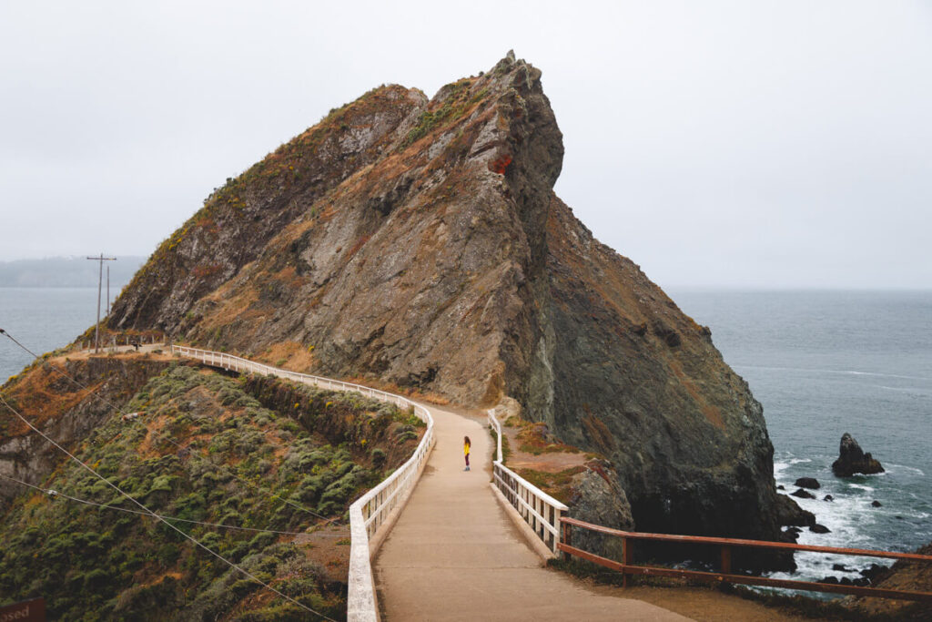 A female tourist standing on Point Bonita Lighthouse trail in front of a huge rock.