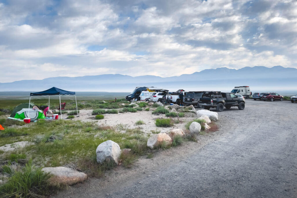 A full parking lot with some tents set up off to the side on a grassy area.