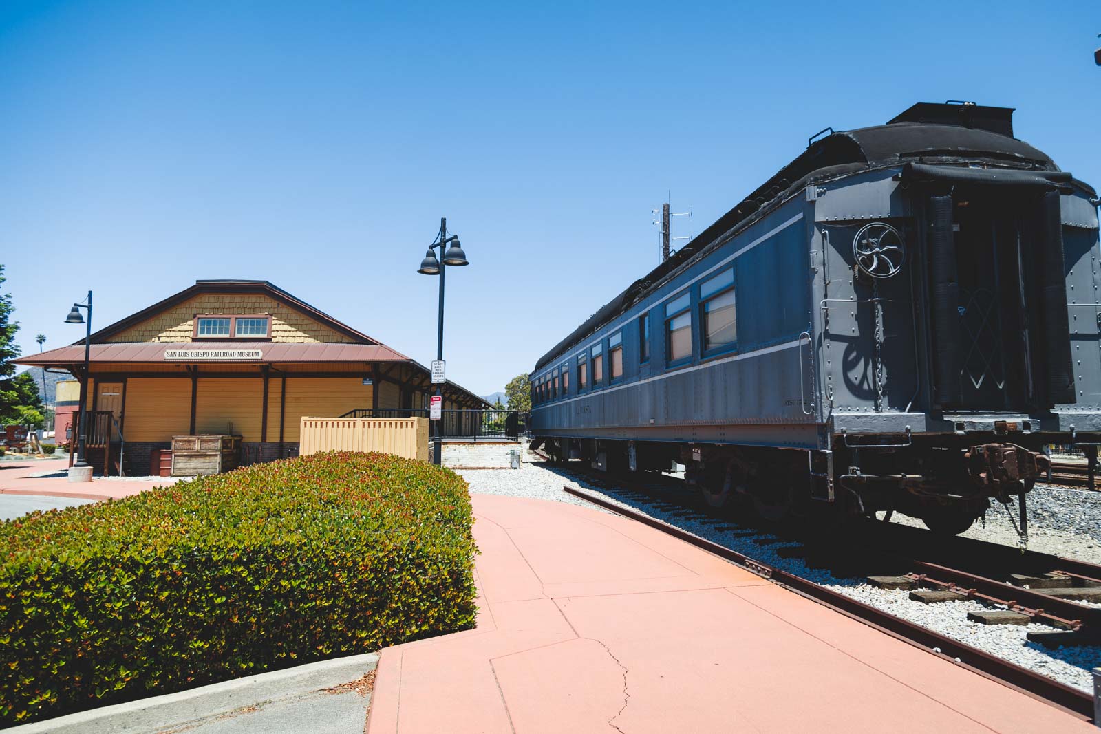 Gray train cart besides San Luis Obispo Railroad Museum on a sunny day.