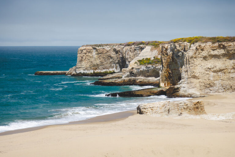 Rough cliffs and blue ocean water at Bonny Doon Beach on a sunny day.