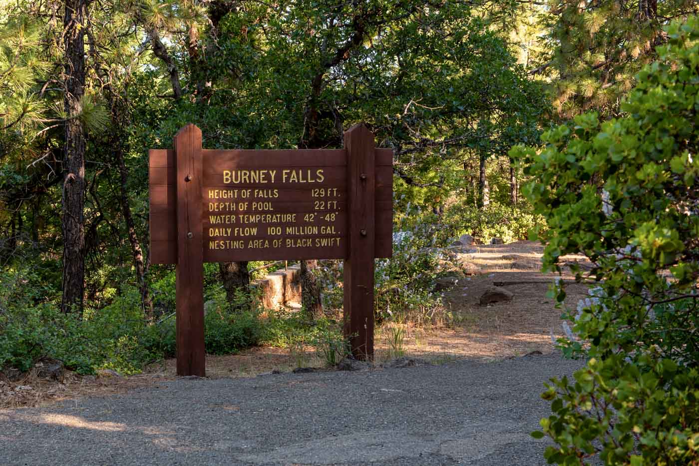 Burney Falls hiking trail and sign. Sign says height of falls at 129ft, Depth of pool at 22ft, and water temperature at 42 to 48 degrees Fahrenheit. 