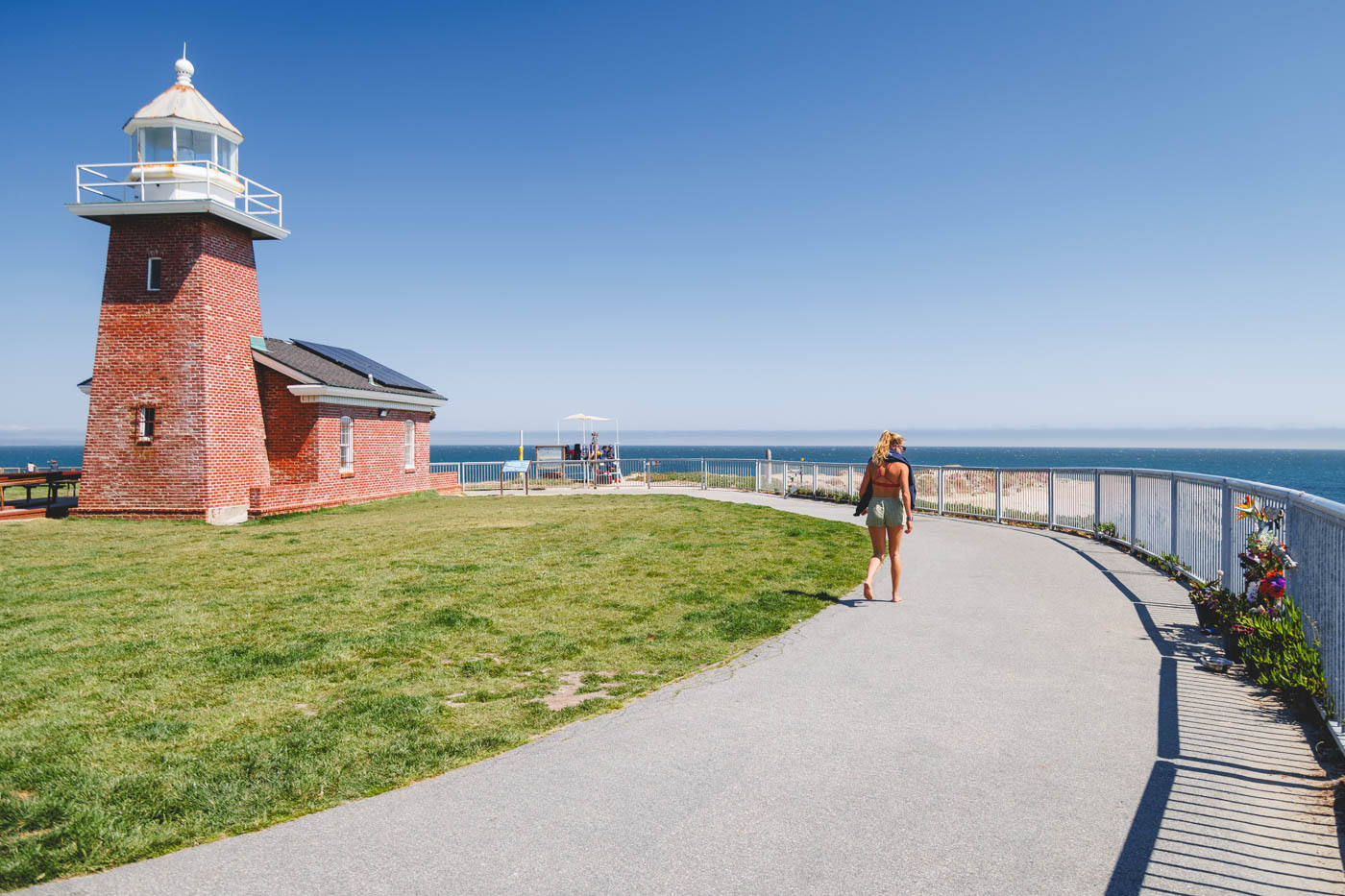 A girl walking along the promenade next to a red brick lighthouse along Lighthouse Point Trail in Santa Cruz.