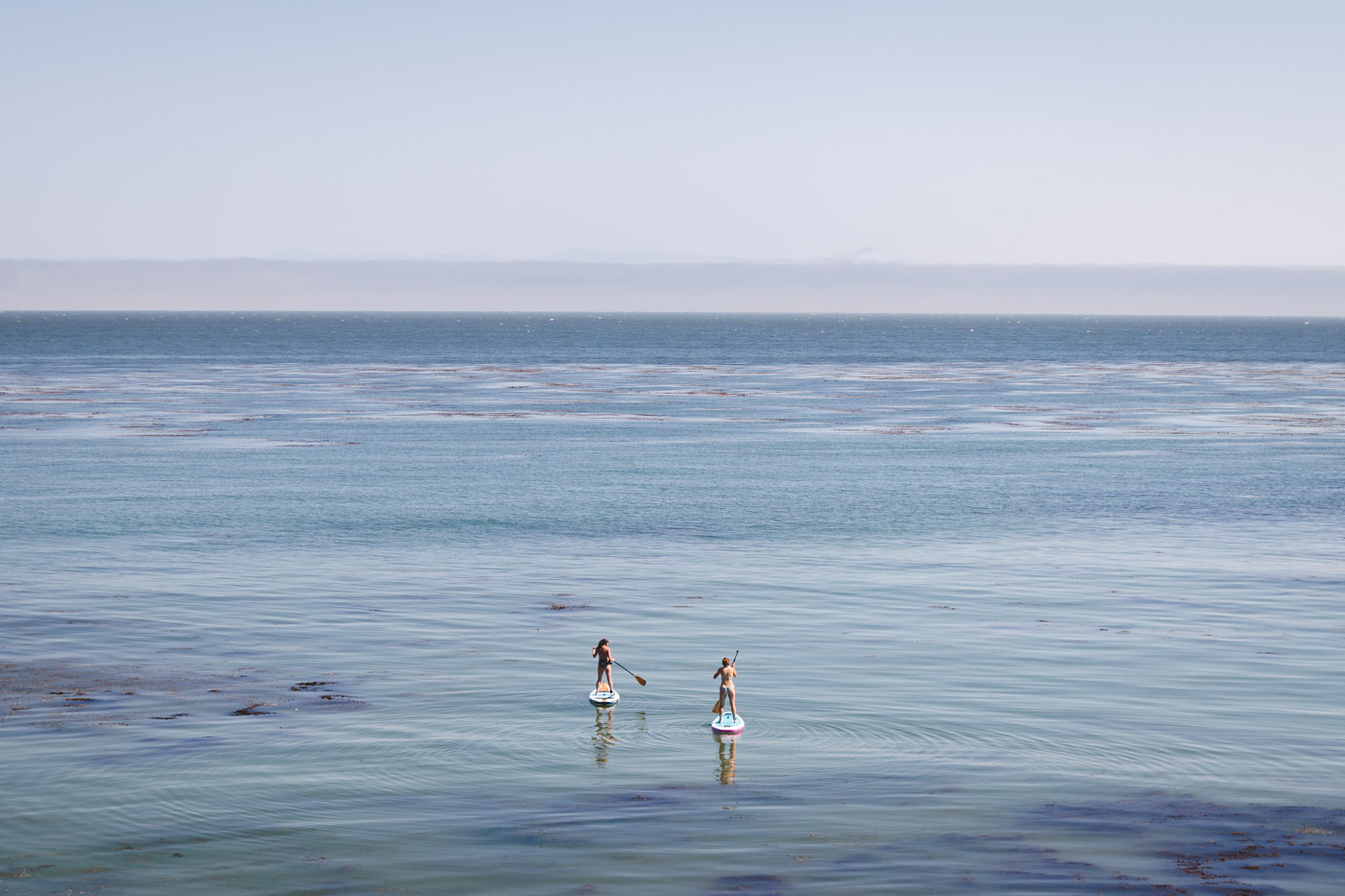 Two girls on stand up paddle boards on the calm ocean waters of Pleasure Point.