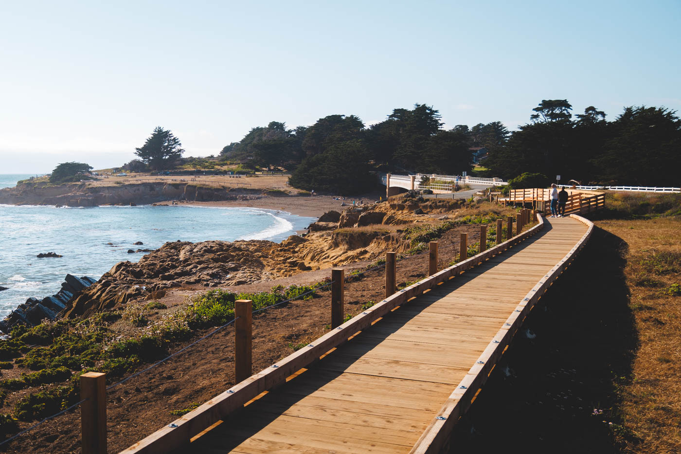 A couple walking down Moonstone Boardwalk towards the beach and bridge at Leffingwell Landing Park near Cambria.