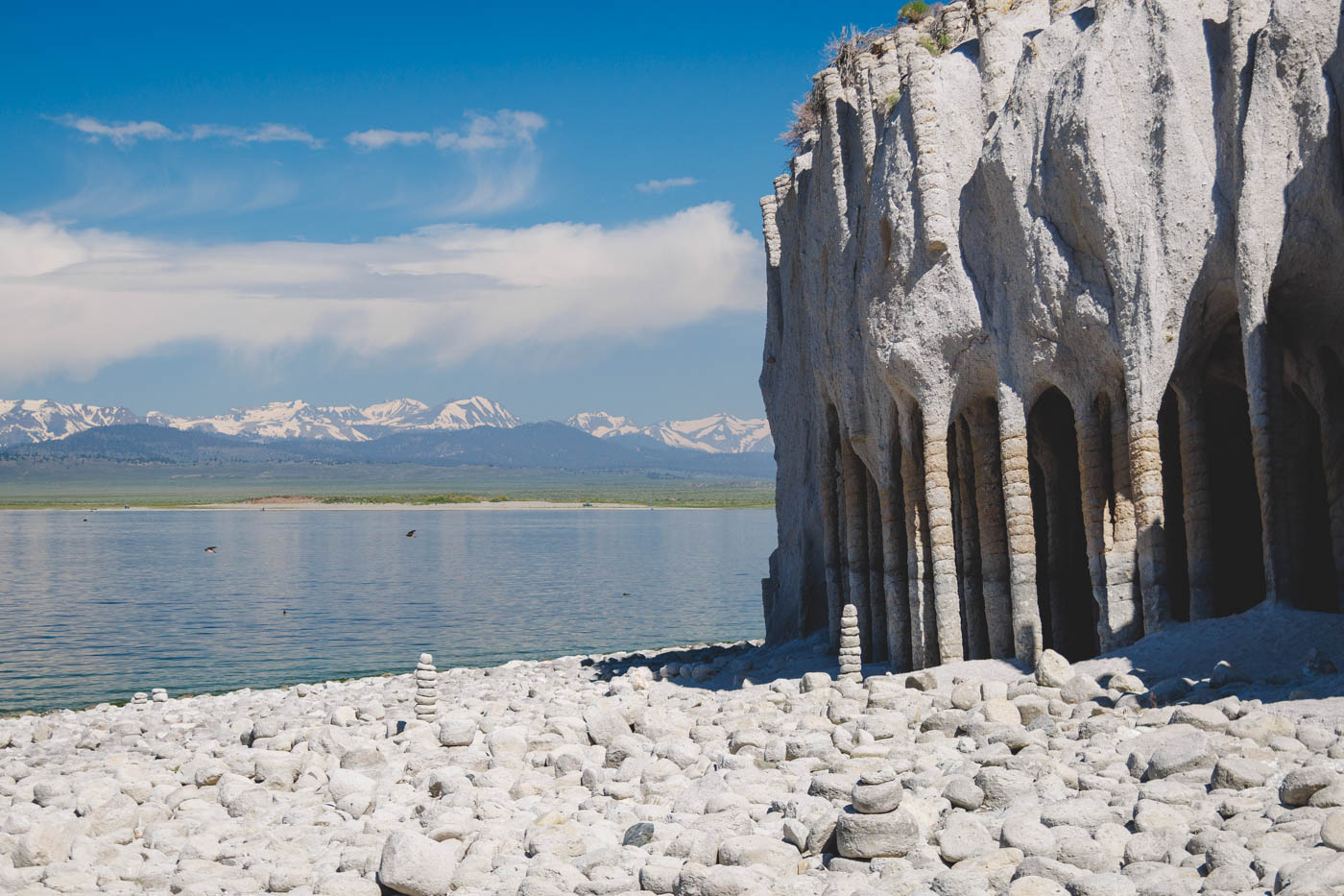 Close up of the Crowley Lake Columns besides the lake with rocks on the shoreline and a view of mountains on a sunny day.