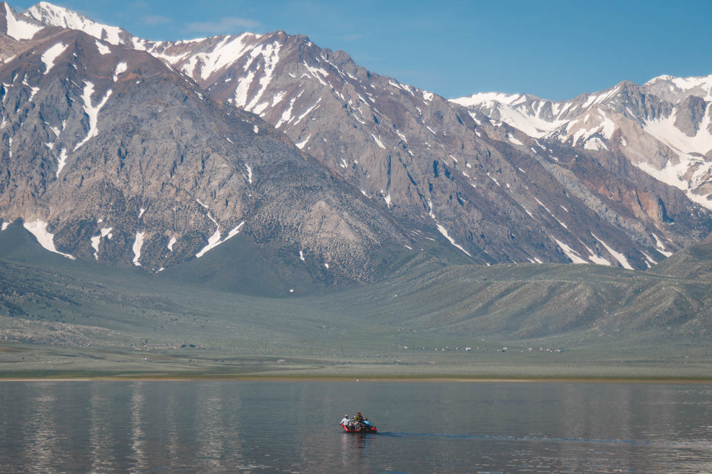 Three people in a red dingy on Crowley Lake with an amazing view of snow-capped mountains.