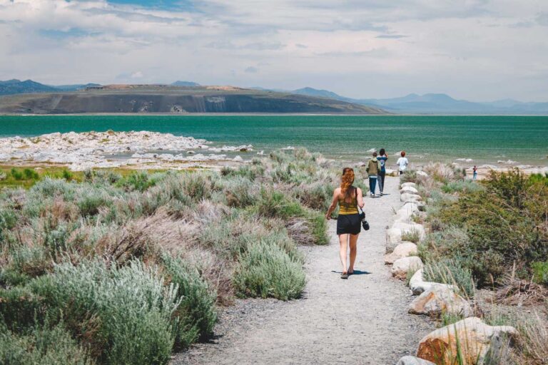 Nina hold a camera and walking along a dirt pathway heading through Tufa State Natural Reserve towards the shores of Mono Lake.