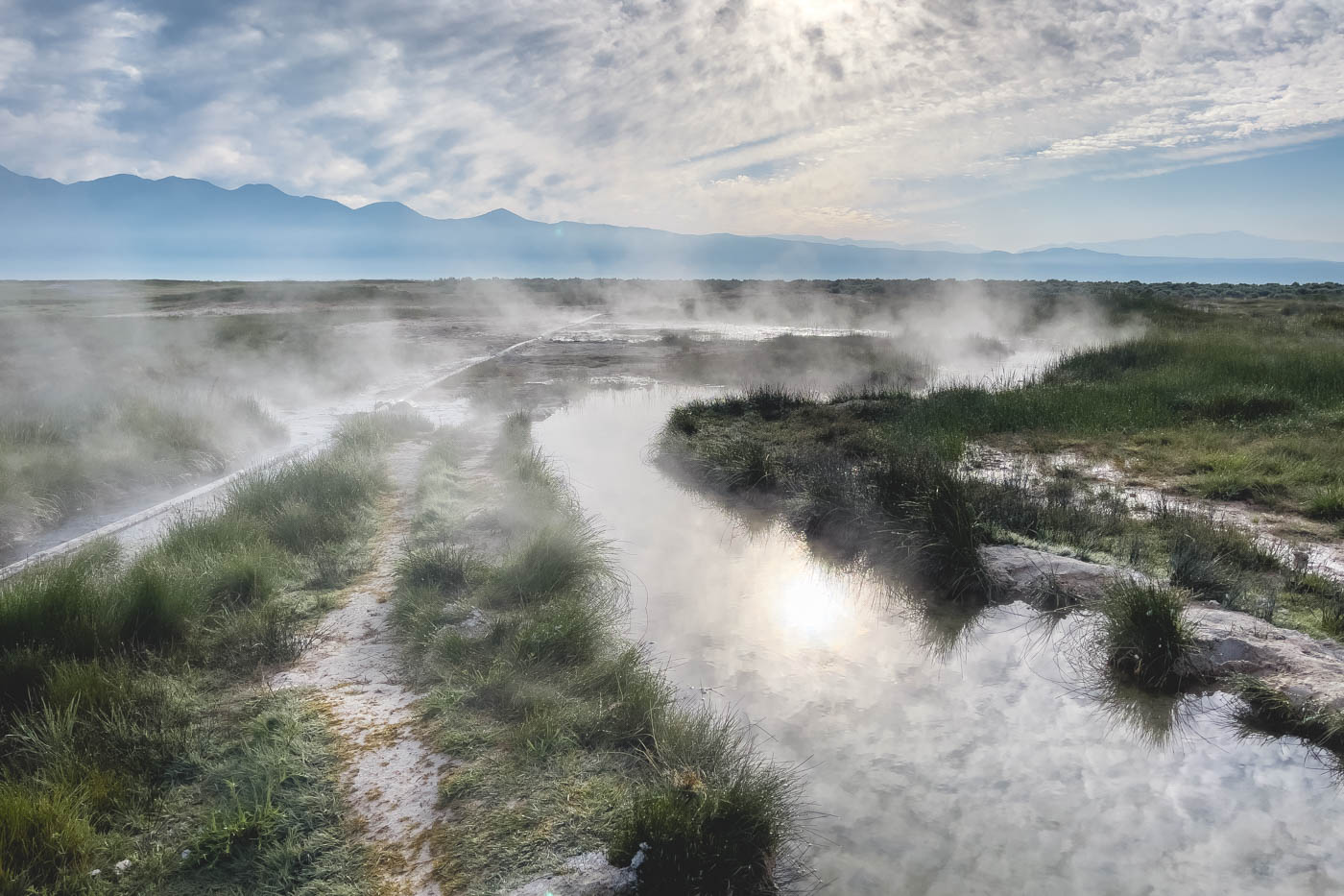 A beautiful scene of steam rising over a stream in a geothermal activity in the area.