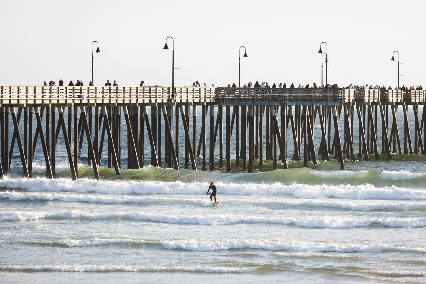 A surfer on the waves besides the pier at Pismo Beach.
