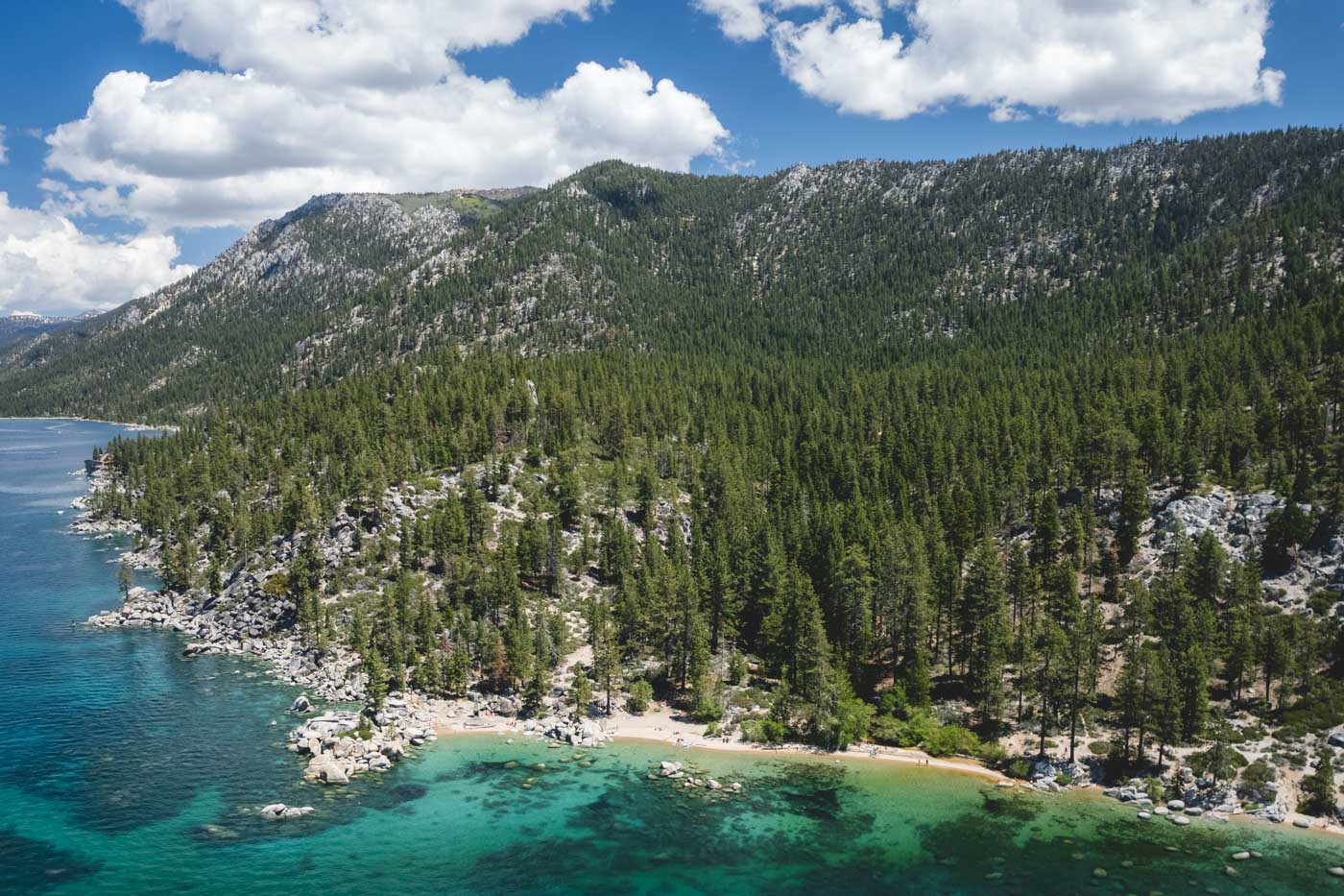 Aerial view over Chimney Beach beside Lake Tahoe with trees covering the mountain.