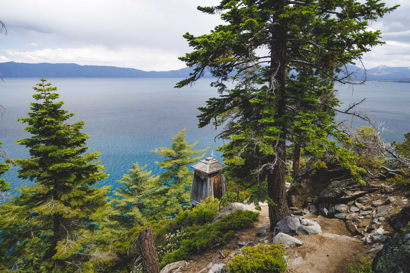 A small wooden antique lighthouse perched on the cliffs along the Rubicon Trail surrounded by trees and the lake.