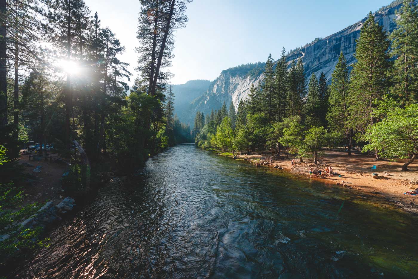 Sunlight shining over a river bordered with trees and mountains at Camp 4 in Yosemite.