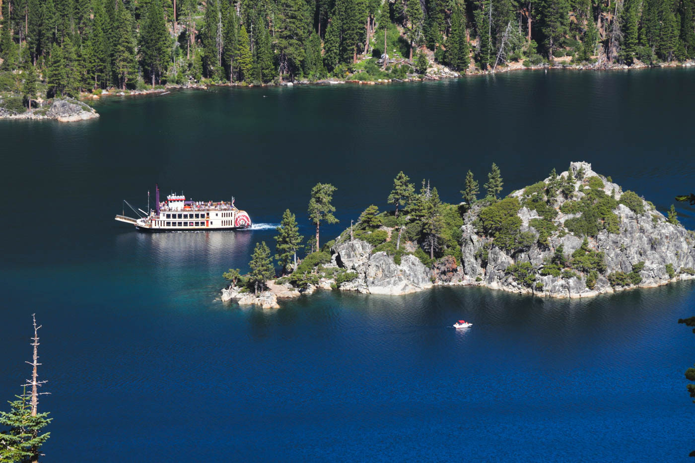 A white cruise boat on Lake Tahoe sailing past a tree-covered Fannette Island.