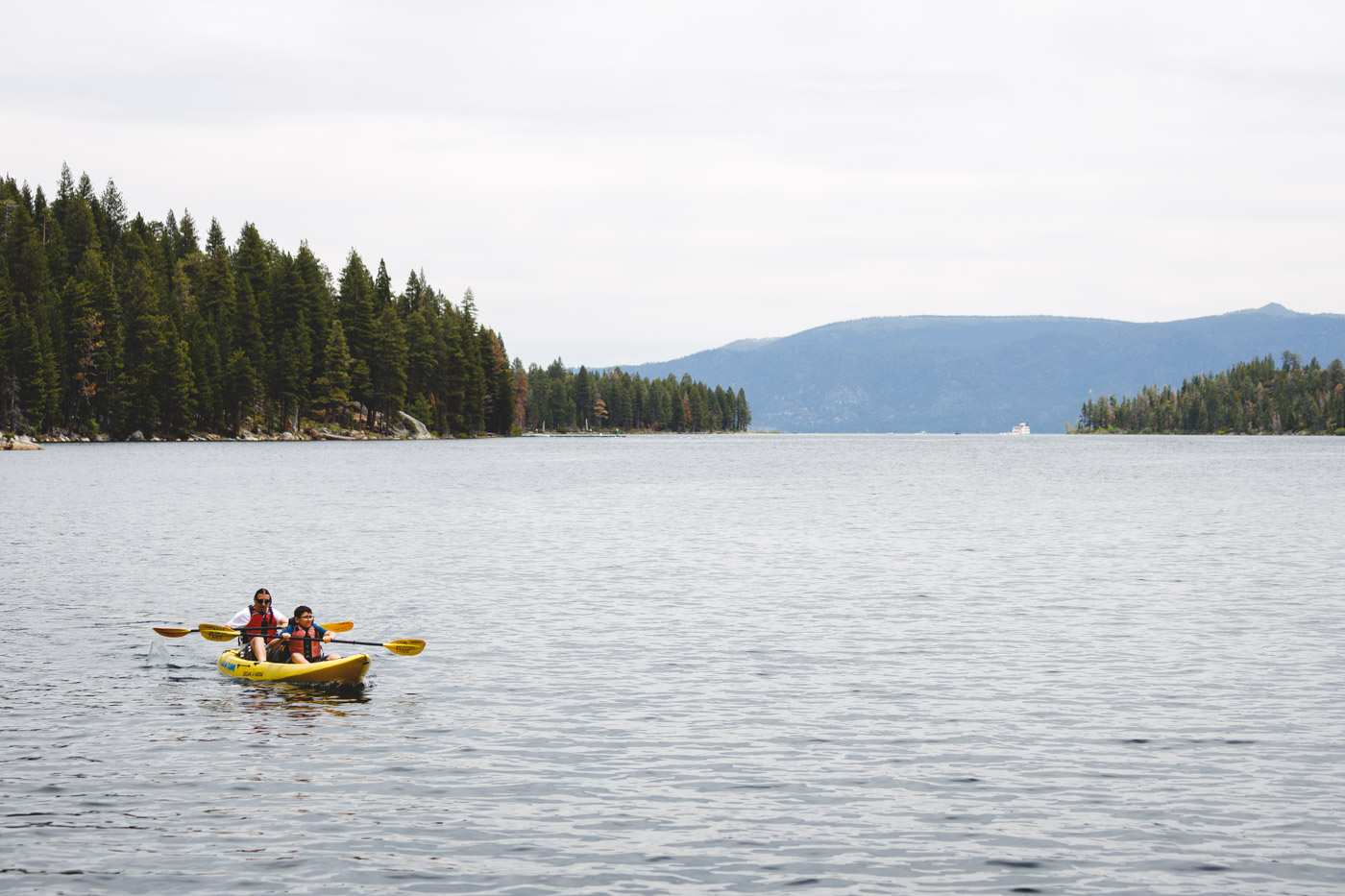 A mother and son in a yellow kayak on Lake Tahoe with trees and mountains in the distance.