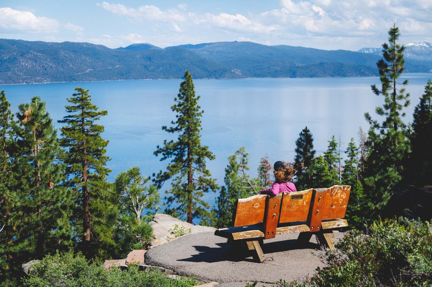 Nina sitting on a wooden bench looking out over Lake Tahoe an it's forests on a sunny day.